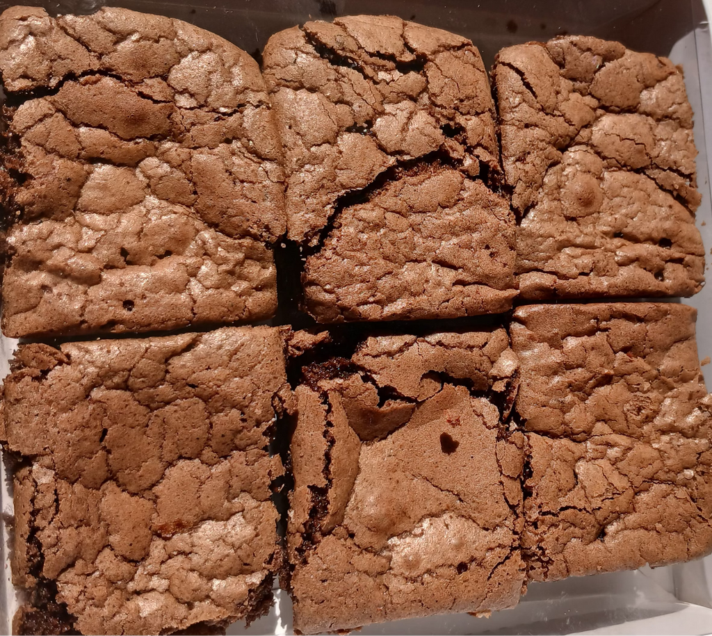 Square box with brownies cut into six pieces on a white surface.