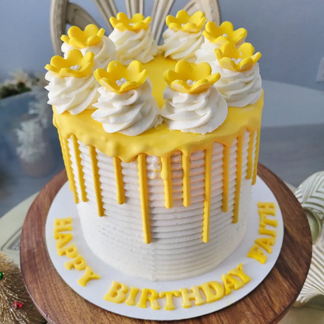 Birthday cake with yellow flowers and white decorations on a wooden stand.