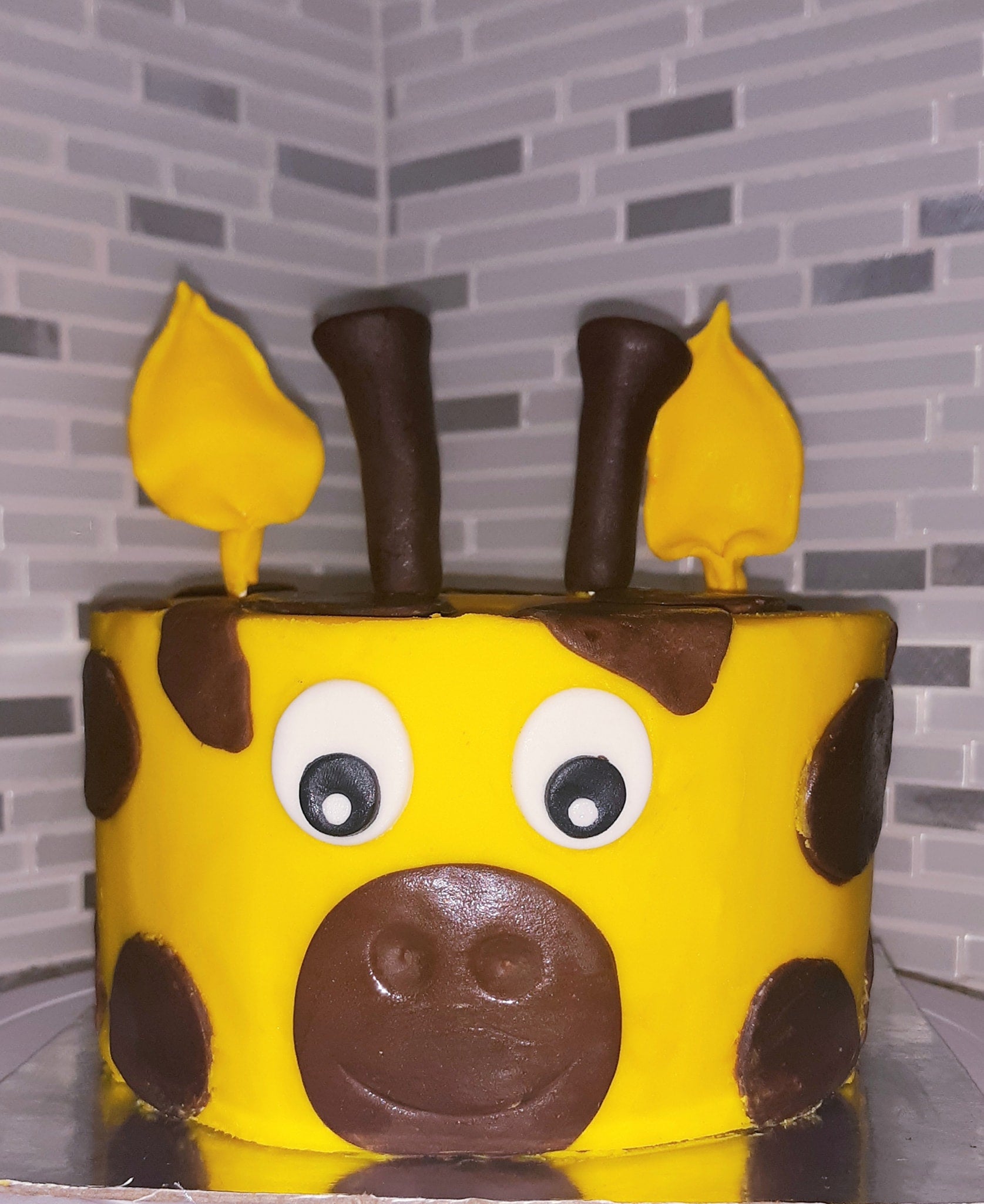 Yellow cake with brown spots and chocolate decorations rese. mbling a giraffe against a tiled wall background