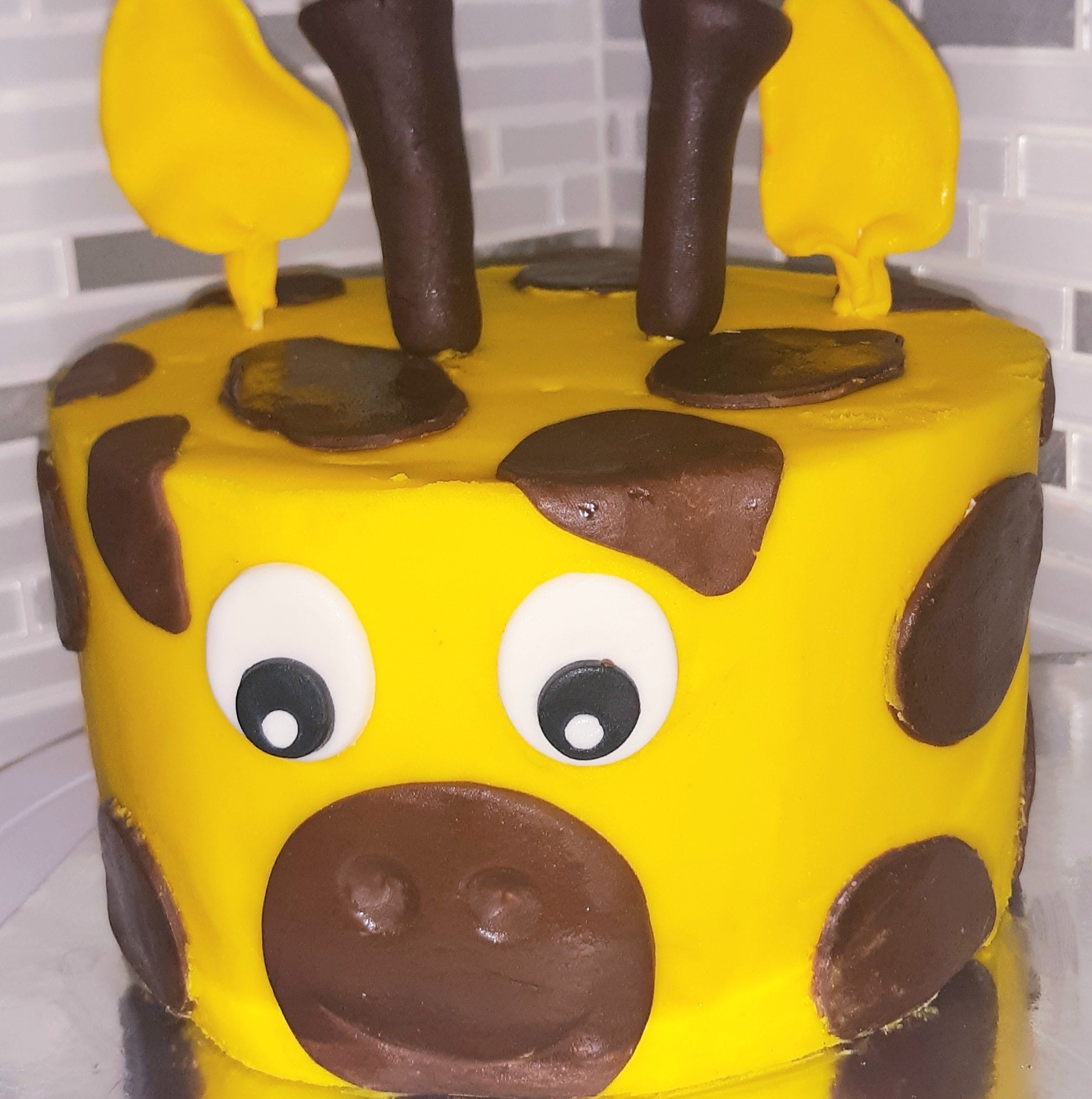 Yellow cake with brown spots and a face on a white surface, Giraffe 3D cake