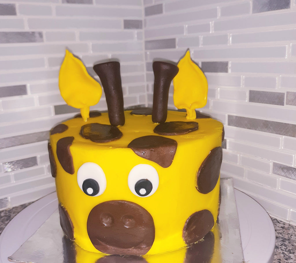 Yellow cake with brown decorations resembling a cow on a white plate against a tiled wall background.