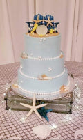 Three-tiered wedding cake with beach-themed decorations on a patterned tablecloth. beach theme wedding cake
