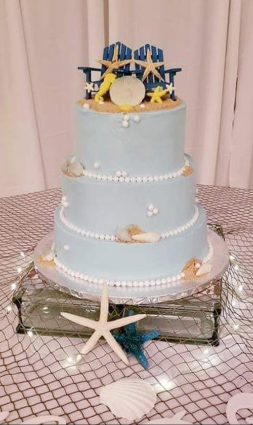 Three-tiered wedding cake with beach-themed decorations on a patterned tablecloth. beach theme wedding cake
