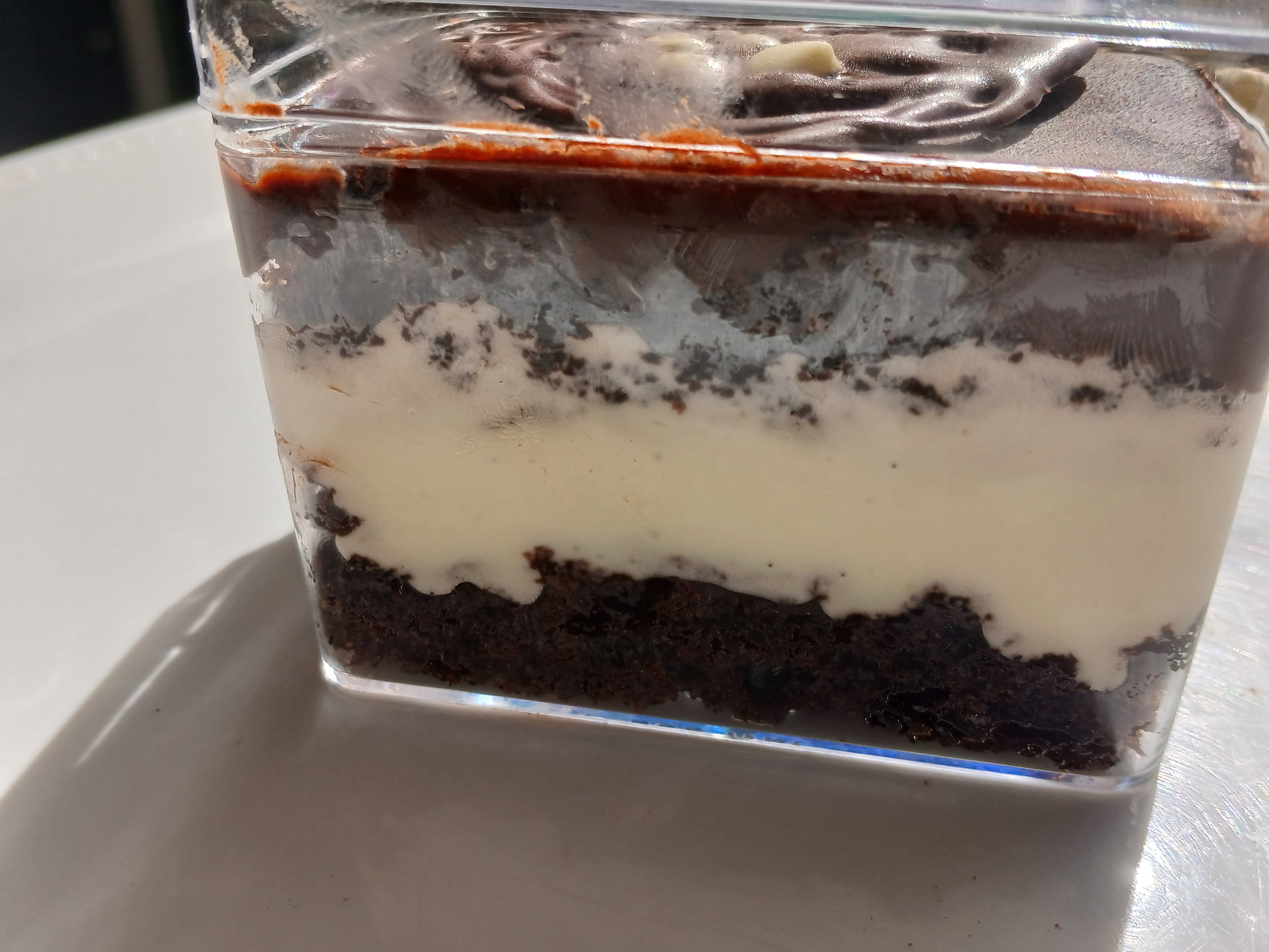 Layered chocolate cake dessert in a clear container on a white surface