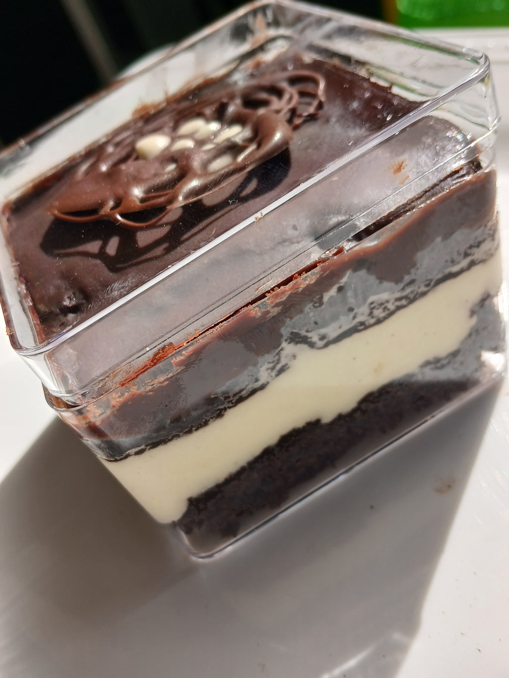 Layered chocolate cake with tiramisu filling dessert in a clear container on a white surface.