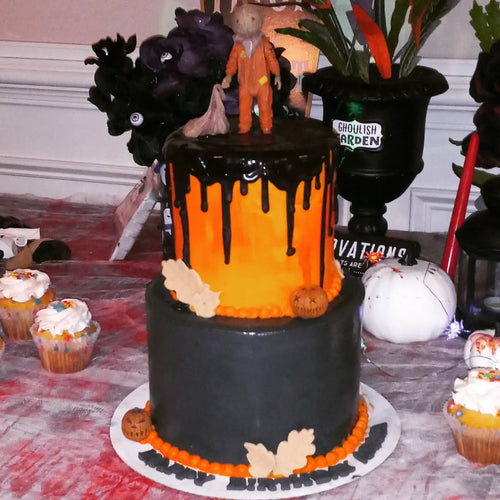 Halloween-themed cake with black and orange decorations on a table with cupcakes.