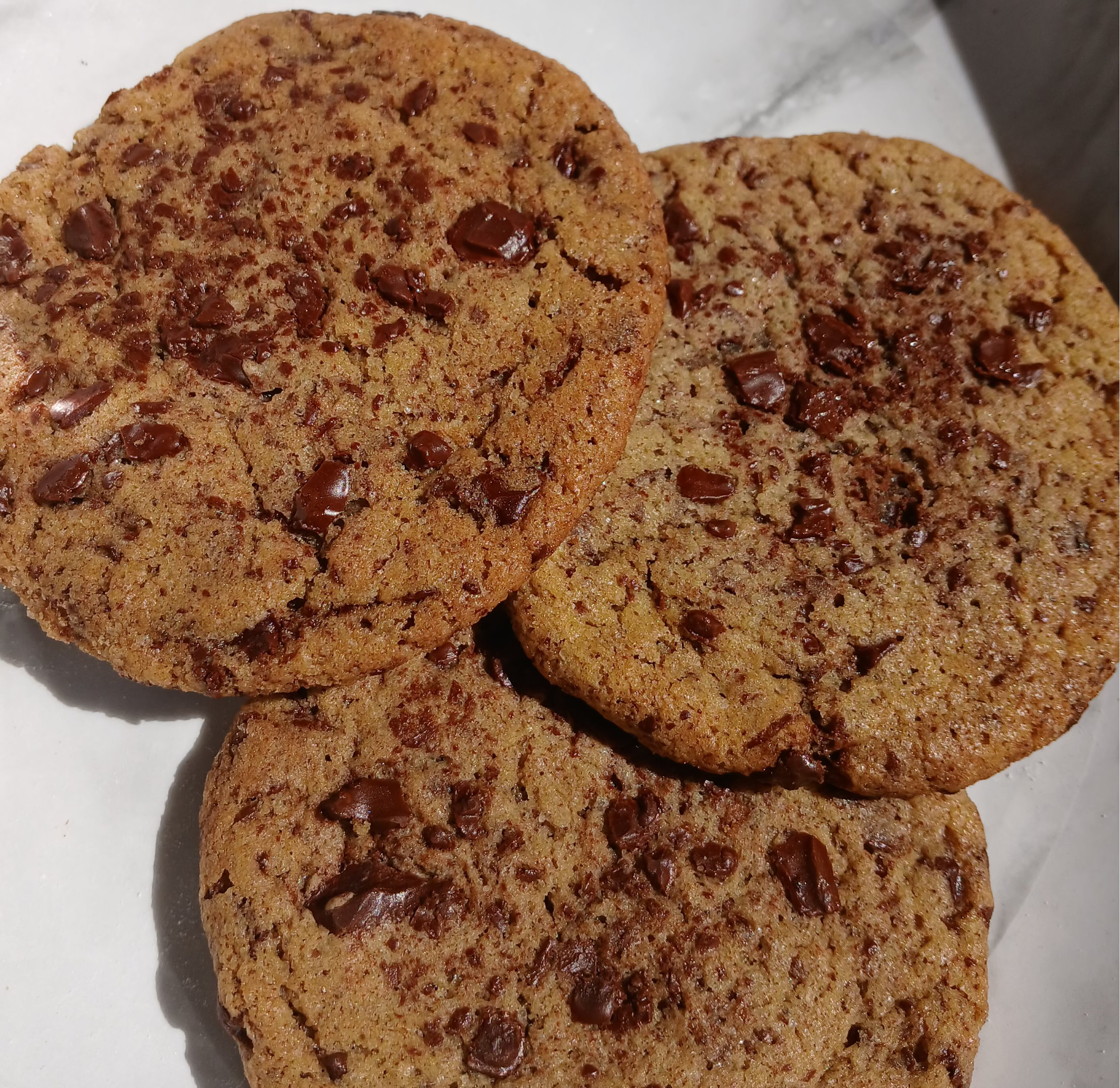 Three chocolate chip cookies on a white surface