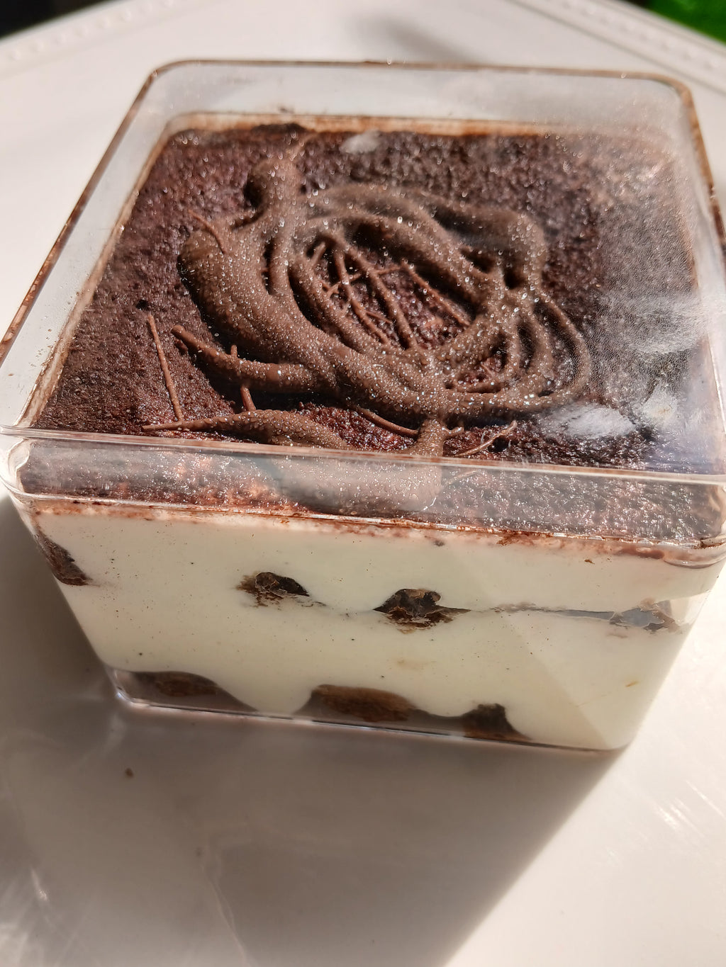 Layered tiramisu dessert in a clear container on a white surface.