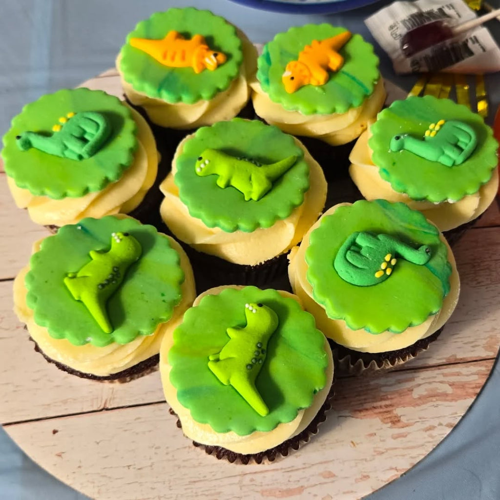 Cupcakes with green frosting and dinosaur decorations on a wooden surface.