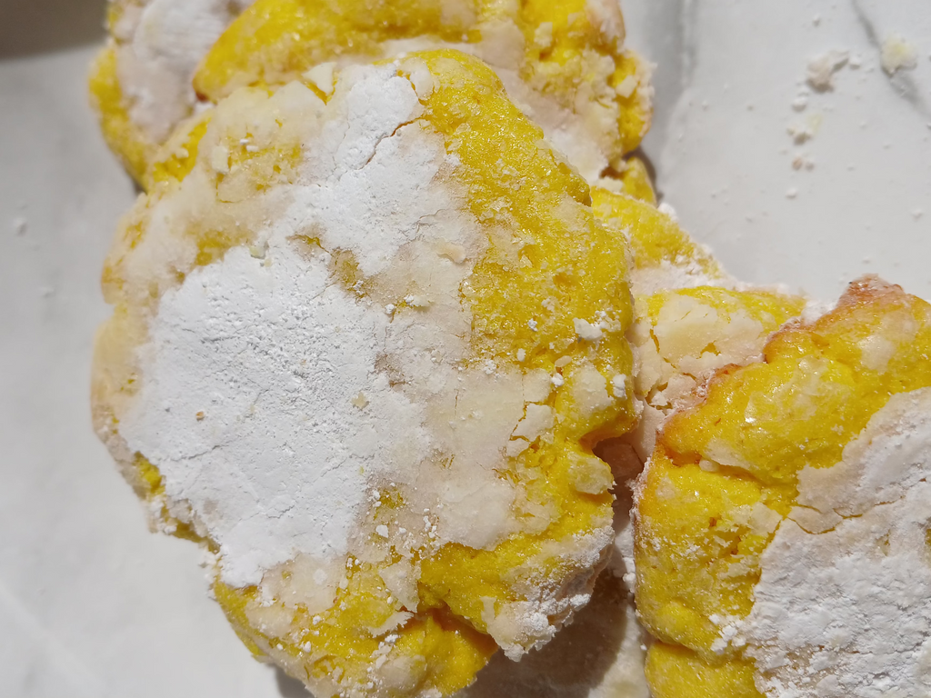 Yellow crinkle cookies with powdered sugar on a white plate