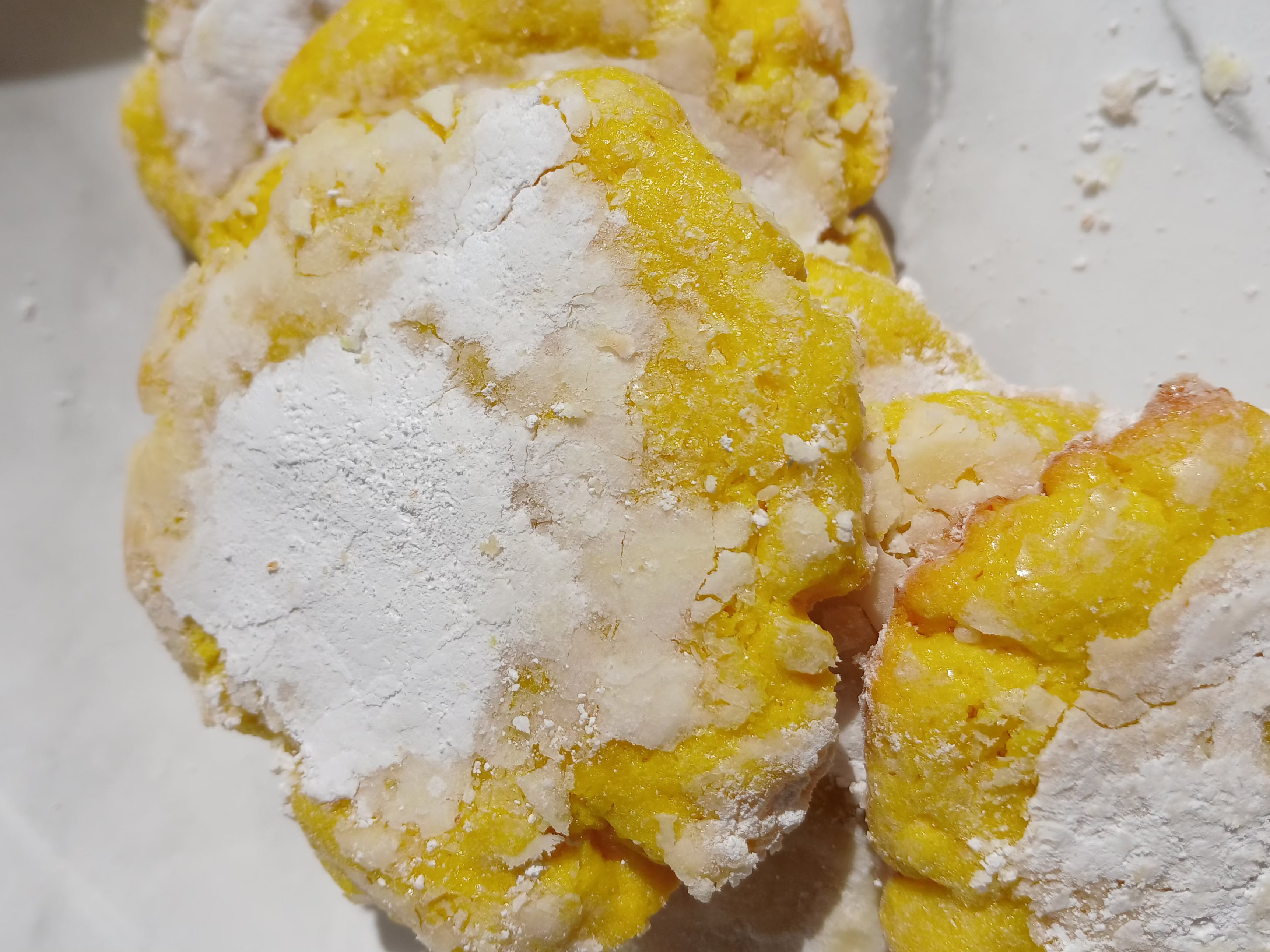 Yellow crinkle cookies with powdered sugar on a white plate