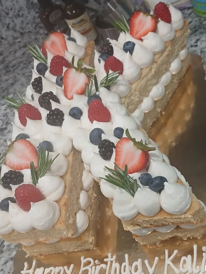 Birthday cake shaped like the number '4' with white frosting, berries, and fresh herb garnishes.