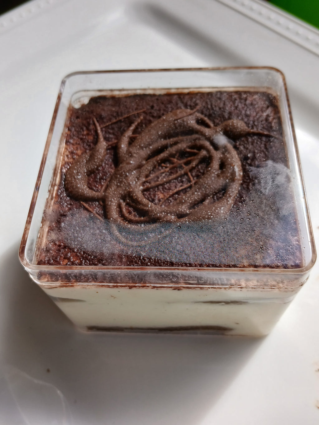 Layered tiramisu dessert in a clear container on a white surface.