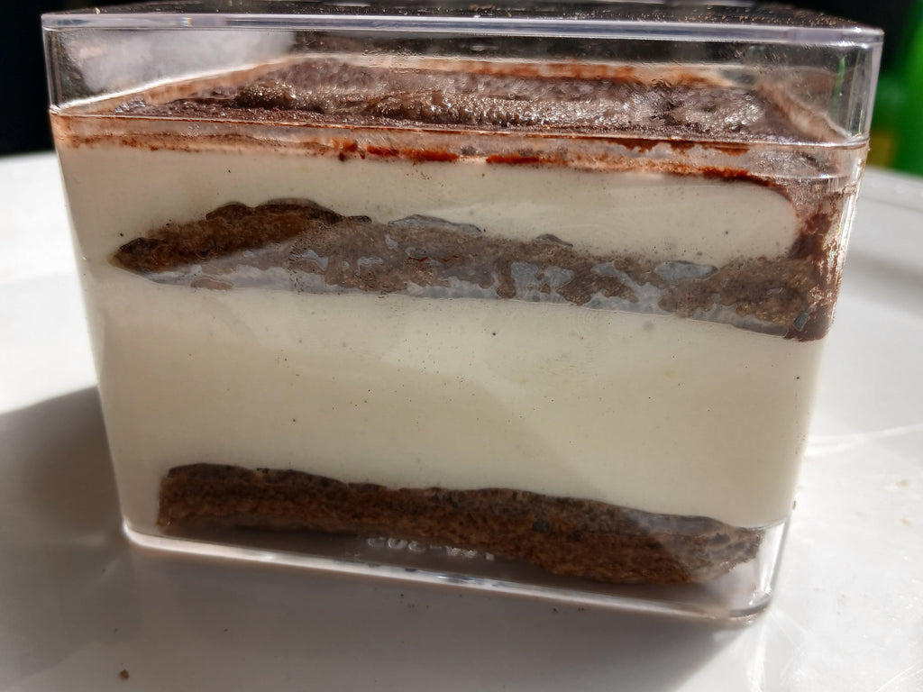 Layered tiramisu dessert in a clear container on a white surface.